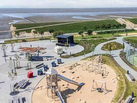 A playground with slides and swings, a covered seating area, and a sandy play zone.