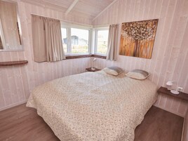 Une chambre à coucher avec un grand lit, une fenêtre avec des rideaux, une tête de lit en bois et un tableau accroché au mur.