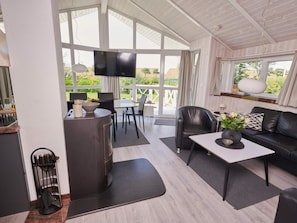 Ein modernes Interieur mit Essbereich, einer Couch, einem Fernseher und Blick ins Freie.