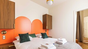 A hotel room with a bed, wooden headboard, orange accent wall, and a wooden nightstand. - Port-royal Residence - Modern Apartement-1br- 4P (Paris)