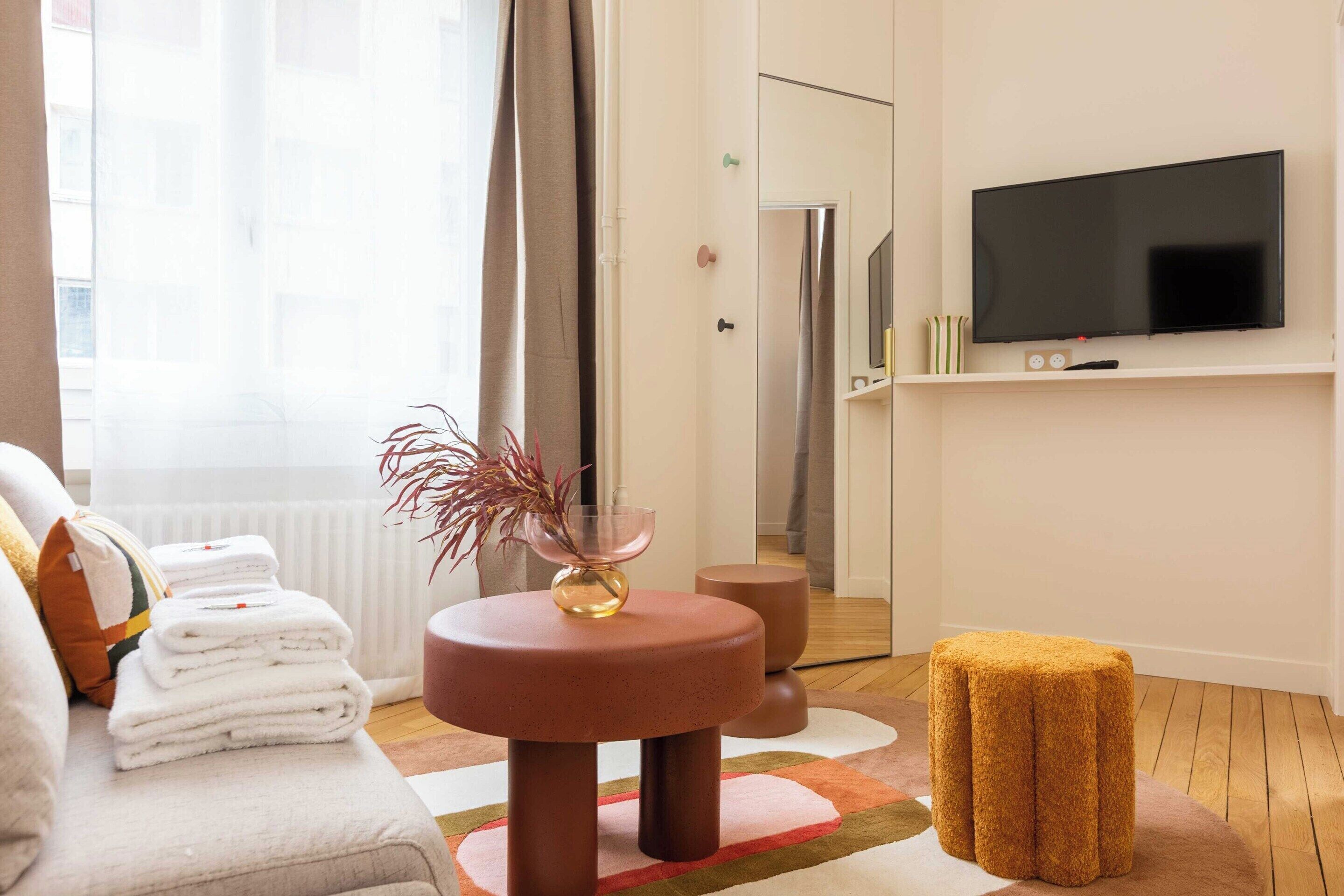 Ein modernes Wohnzimmer mit einer Couch, einem Couchtisch, einem an der Wand befestigten Fernseher und Blick ins Freie durch ein Fenster.