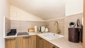 A compact kitchen with wooden cabinets, a white sink, and a countertop with a kettle and utensils. - Port-royal Residence - Modern Apartement-1br- 4P (Paris)
