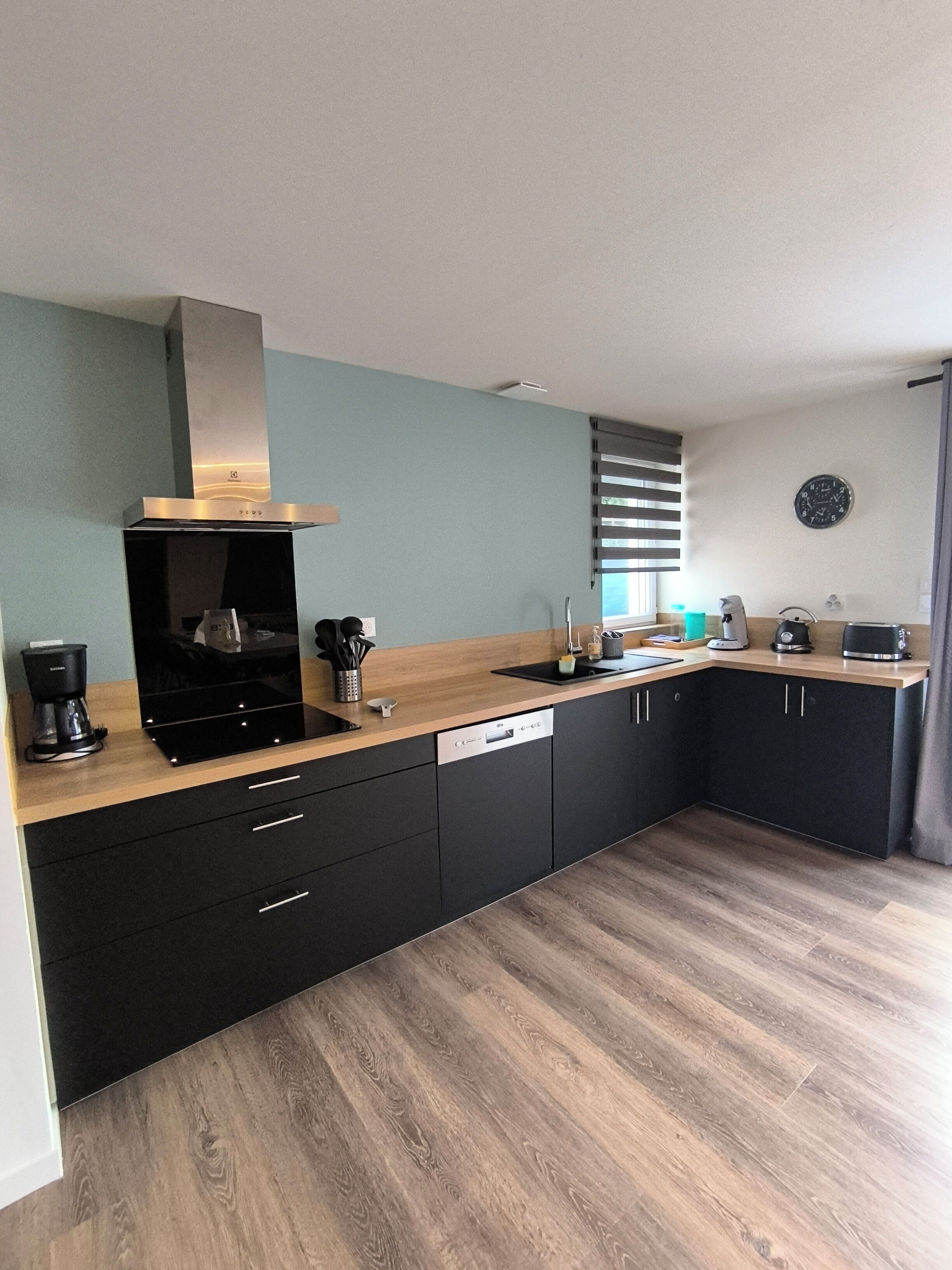 Una cocina moderna con gabinetes negros, encimera de madera, horno empotrado y cafetera.
