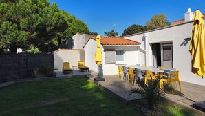 A patio with a table and chairs, a yellow umbrella, and a small garden area. - Vacation home - 9 people - "Relax à Sion" between sea and forest (Saint-Hilaire-de-Riez)