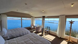 A hotel room with two beds, a small table, a chair, and a view of the sea. - Uros Maya lodge (Puno)