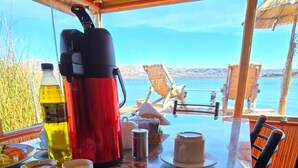 A dining table with a plate of food, a kettle, and a bottle of olive oil. - Uros Maya lodge (Puno)