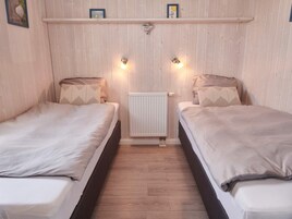 A room with two beds, a radiator, and wall-mounted lights.