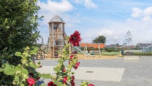 Ein Spielplatz mit einer hölzernen Kletterkonstruktion, einer Schaukel und einer Rutsche.