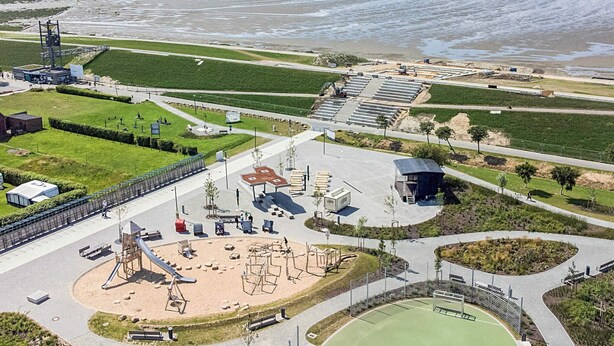 Eine Luftaufnahme eines Küstenparks mit Spielplätzen, Sportfeldern und einem Strand.