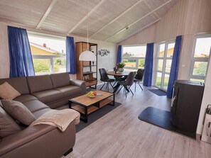 A furnished living area with a sofa, dining table, chairs, a coffee table, a bookshelf, and a television. - 4 Star Holiday Home in Friedrichskoog (Friedrichskoog)
