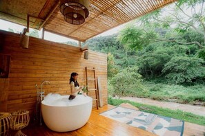 Uma cabana de madeira com uma banheira grande cheia de espuma, uma escada e vista para uma floresta exuberante.
