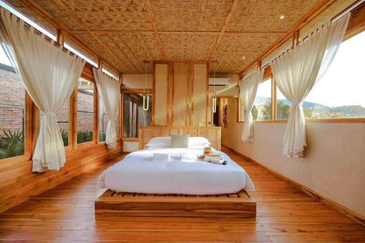 Une chambre spacieuse avec un grand lit, un plancher en bois et de grandes fenêtres dotées de rideaux.