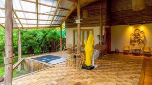 A covered outdoor area with a wooden floor, wicker furniture, and a yellow sculpture.