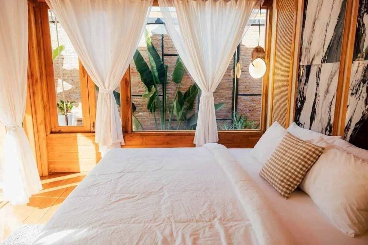 Une chambre avec un grand lit, des rideaux blancs et une vue sur la verdure à l’extérieur.