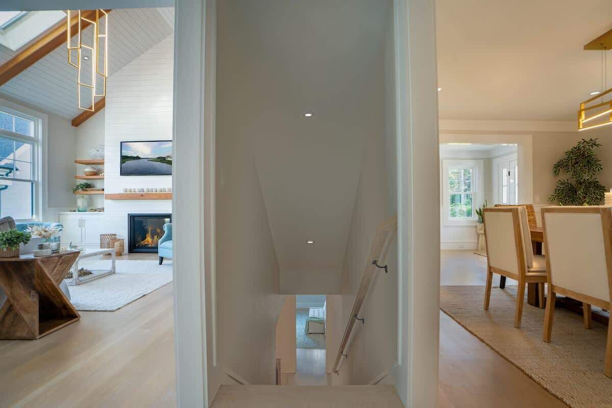 Una escalera conduce a un comedor con vistas al exterior, una chimenea y un televisor en la pared.