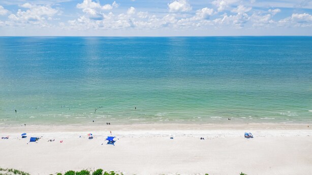 Een strand met helder turquoise water, een zandstrand en enkele parasols.