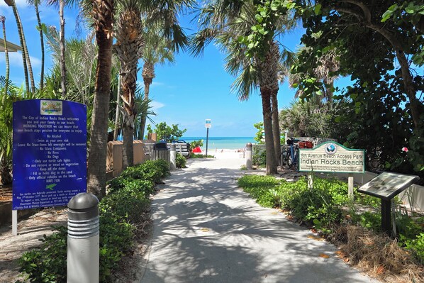 Ein Weg, der zu einem Strand mit Palmen und einem Hinweisschild für den Strandanschluss führt.
