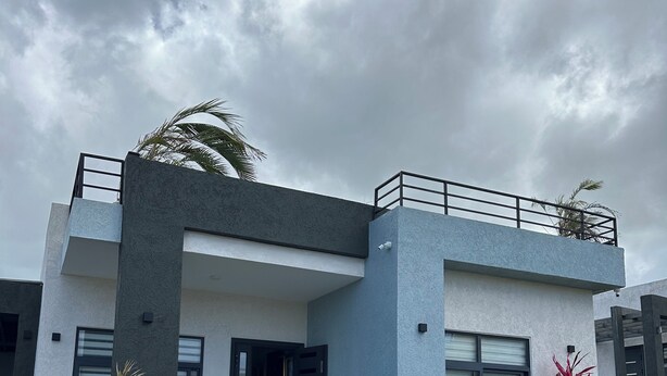 Un edificio moderno a due piani con un balcone, piante in vaso e un giardino curato.