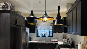 Una cucina moderna con mobili scuri, un'isola centrale con posti a sedere, luci a sospensione e un frigorifero in acciaio inossidabile.