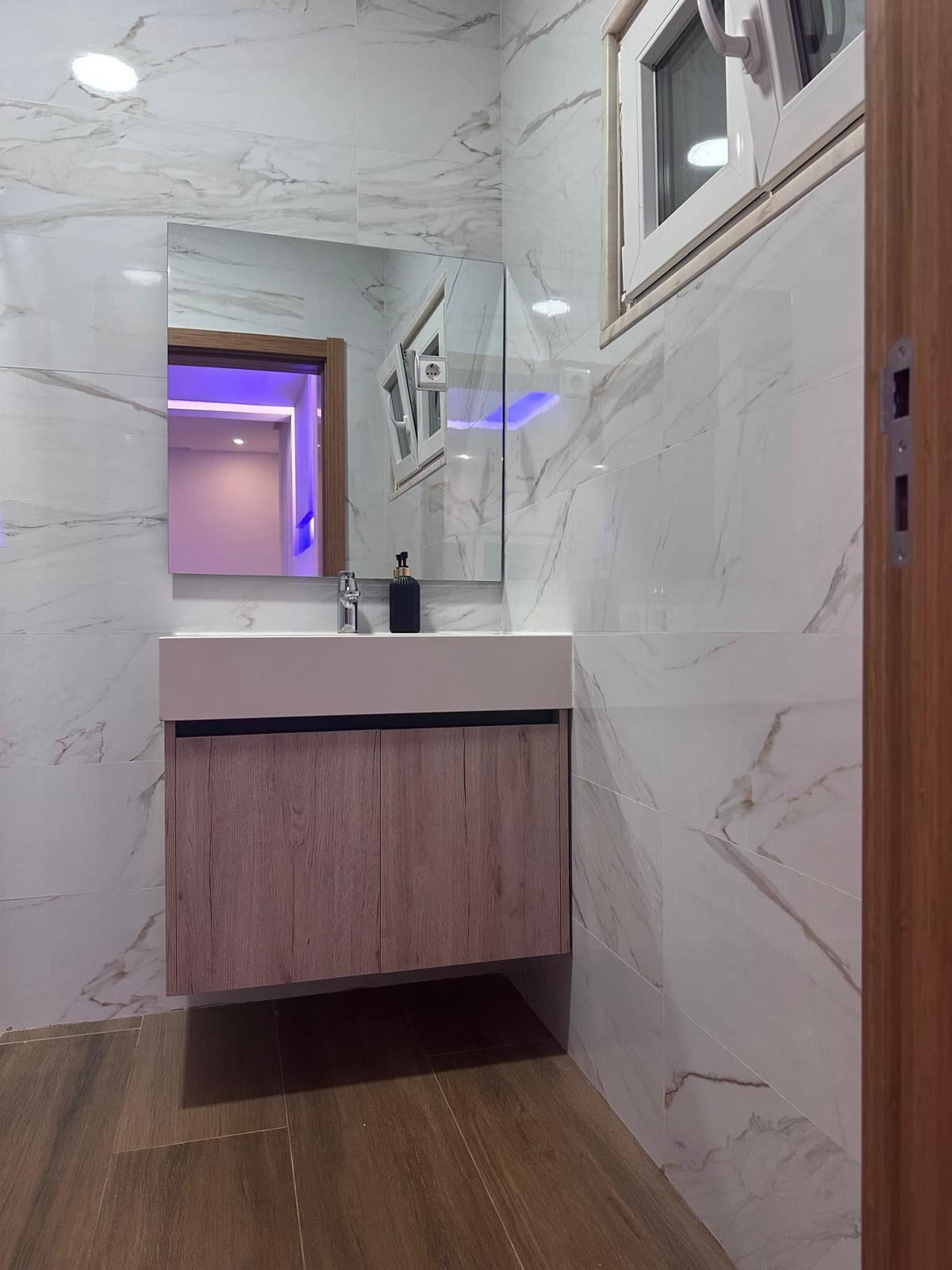 A bathroom with a marble vanity, a wooden cabinet, and a mirror.
