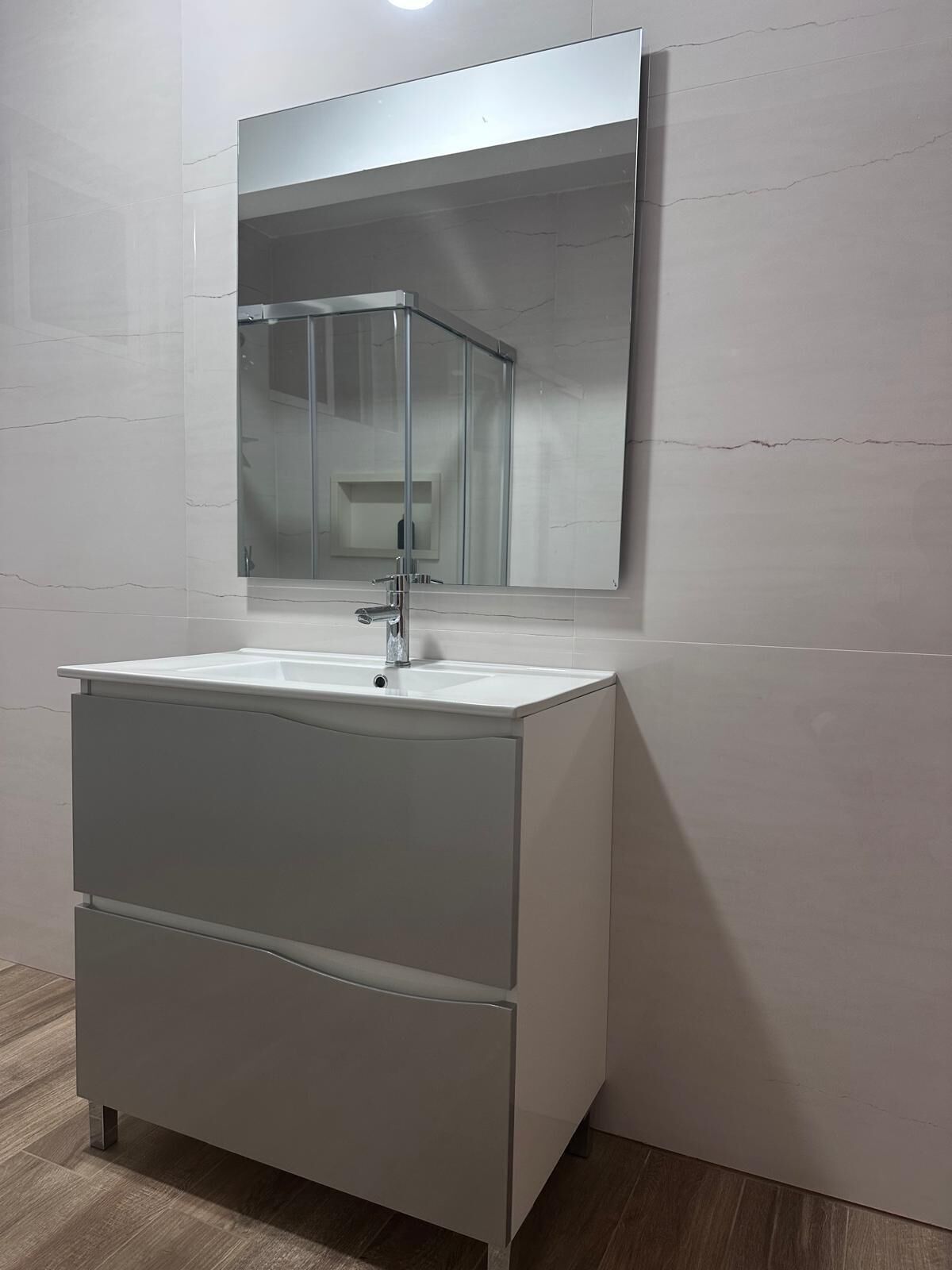 A modern bathroom with a white vanity, a mirror, and a glass shower enclosure.