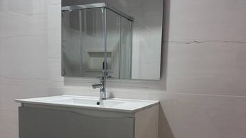 A modern bathroom with a white vanity, a mirror, and a glass shower enclosure.