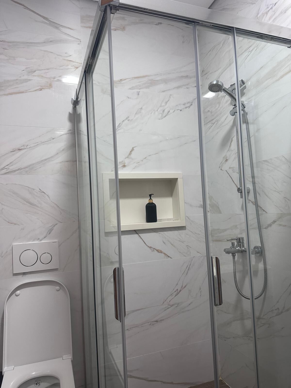 Une salle de bain moderne avec une douche à parois de verre, des murs en marbre et un lavabo sur pied blanc.