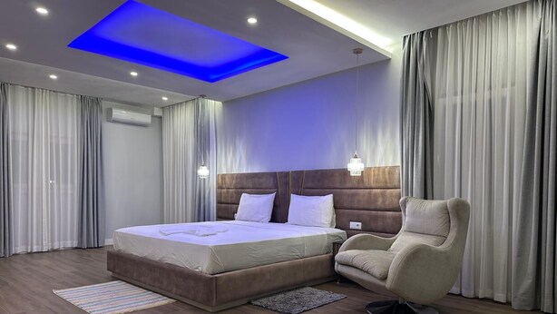 A modern hotel room with a large bed, a chair, and a ceiling light. - Alojamento Santos Silva  (São Tomé)