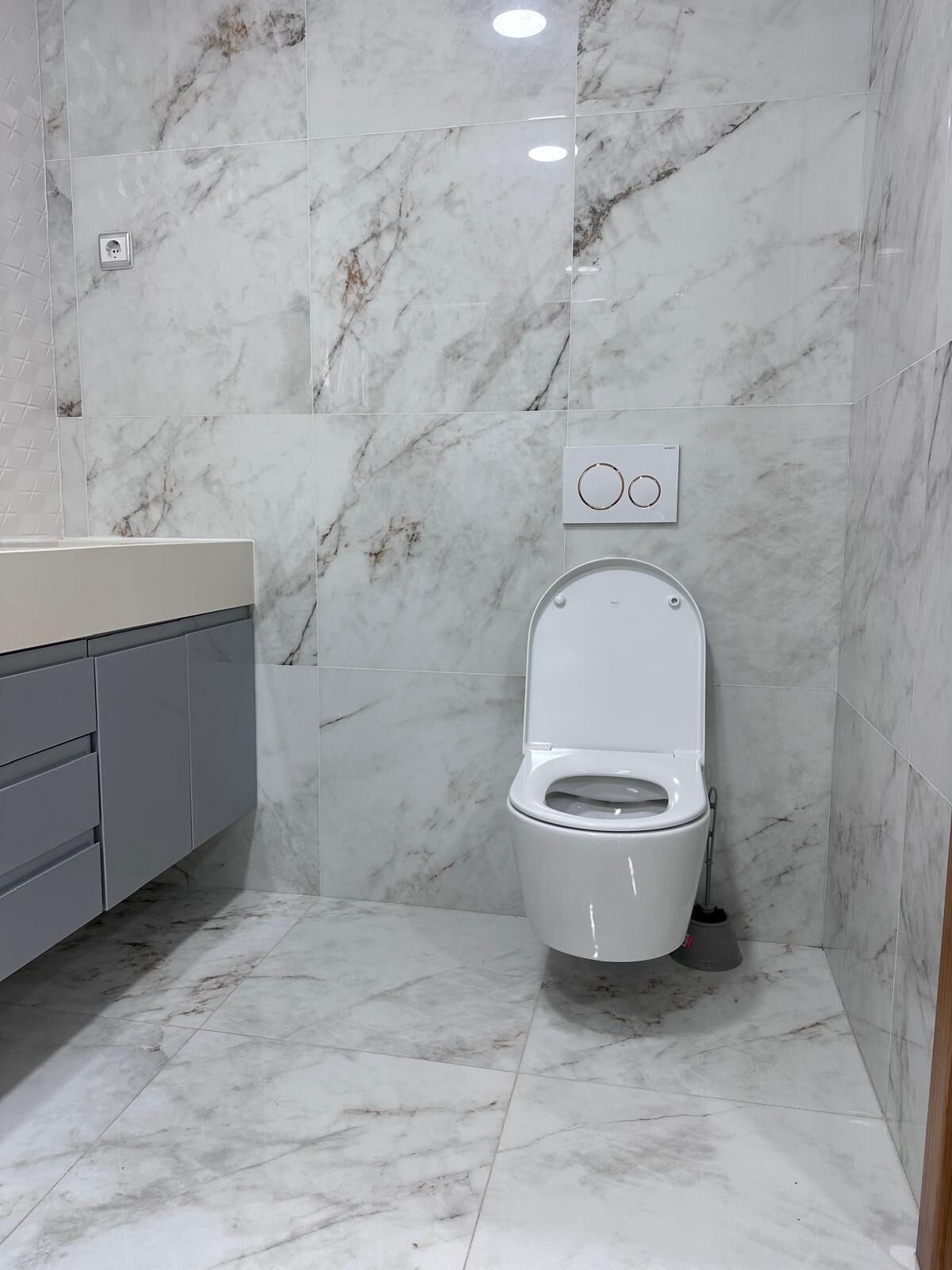 Un baño con inodoro, tocador con encimera y paredes de mármol.