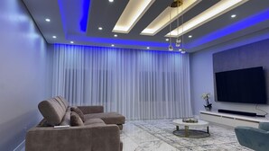 A modern living room with a sectional sofa, a flat-screen TV, and a marble floor. - Alojamento Santos Silva  (São Tomé)