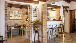 A rustic kitchen with exposed brick walls, wooden beams, a bar area with stools, and a dining table with chairs.