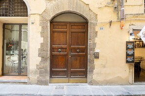 A double wooden door with a stone archway, a glass door with chairs outside, and a sign with restaurant names. - Renaissance Tower Apartment (Firenze)