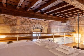 A room with a bed, wooden beams, stone walls, and a hanging light fixture. - Renaissance Tower Apartment (Firenze)