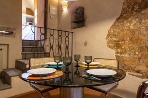 Un comedor con una mesa redonda de vidrio, cuatro sillas y una pared de piedra.