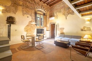 A spacious living area with a stone wall, a round table with chairs, a sofa, and a coffee table. - Renaissance Tower Apartment (Firenze)