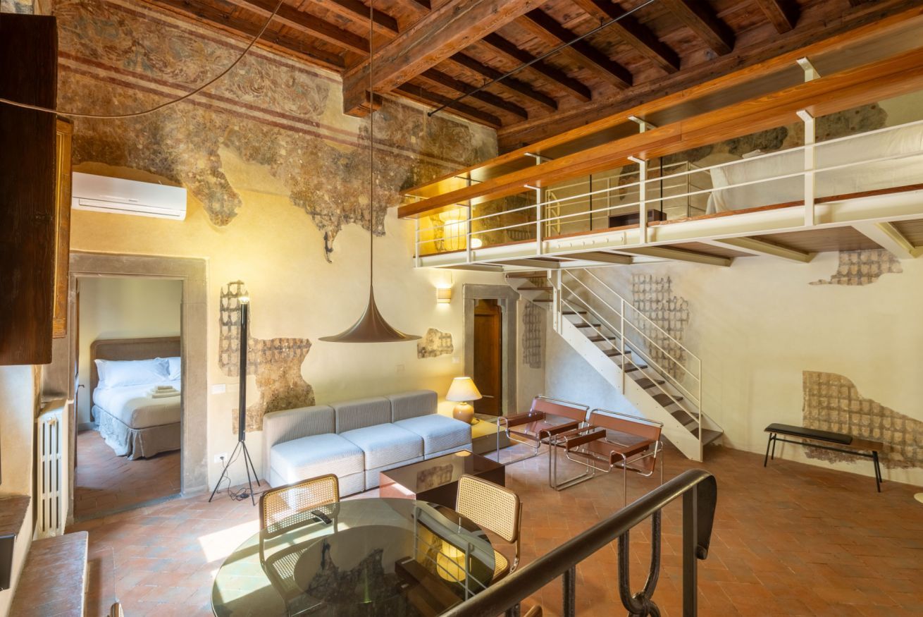 Un espacio habitable amplio con techo alto, vigas de madera a la vista, una escalera y un balcón.