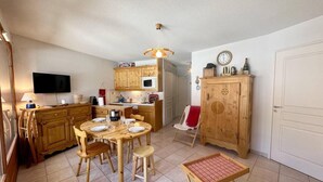 A compact kitchen with wooden cabinets, a dining table, and a television.