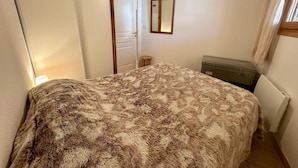 A bedroom with a large bed, a mirror on the wall, a radiator, and a suitcase.