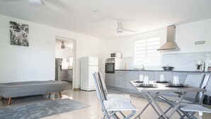 A modern kitchen with white appliances, a dining area with a table and chairs, and a gray sofa. - Villa Angerville, spacious villa that can accommodate up to 24 people (Le Moule)