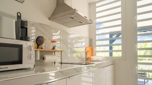 A modern kitchen with white cabinetry, a Brandt microwave, a stainless steel range hood, and a window with blinds. - Villa Angerville, spacious villa that can accommodate up to 24 people (Le Moule)