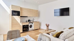 Una cocina moderna con electrodomésticos integrados, un televisor de pantalla plana y una zona de comedor con sofá y mesa.