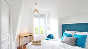 A bedroom with a bed, a desk, a chair, and a window.