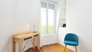 A room with a wooden desk, a blue chair, a window with blinds, and a white wall.