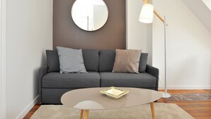 A modern living room with a grey sofa, a round mirror, a floor lamp, and a glass coffee table.