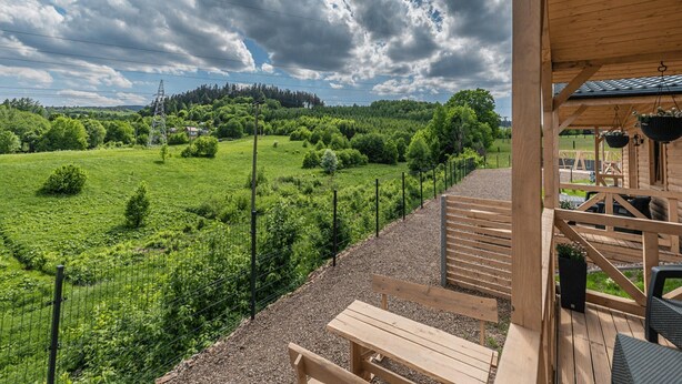 A wooden deck with benches overlooking a green field and a forested hill. - Cottage in Duszniki Zdroj With Panoramic View (Szczytna)