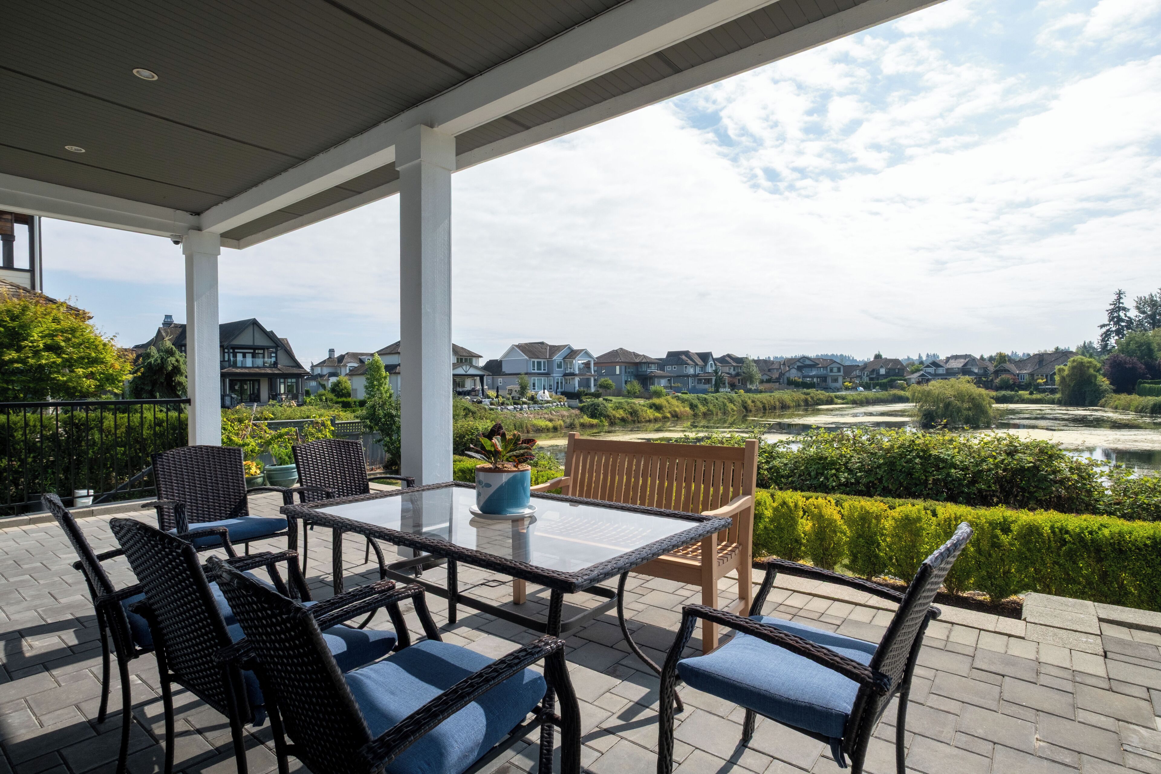 Überdachte Terrasse mit Tisch und Stühlen, mit Blick auf ein Wohngebiet und einen Fluss.