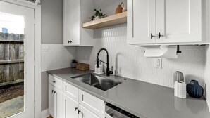 A modern kitchen with white cabinets, a stainless steel sink, and a wooden shelf with decorative items.