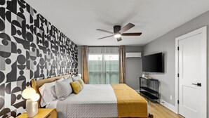 A modern bedroom with a wooden bed, a ceiling fan, a TV, and a patterned wall.