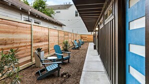 A covered outdoor patio with Adirondack chairs, a concrete path, and a wooden fence.