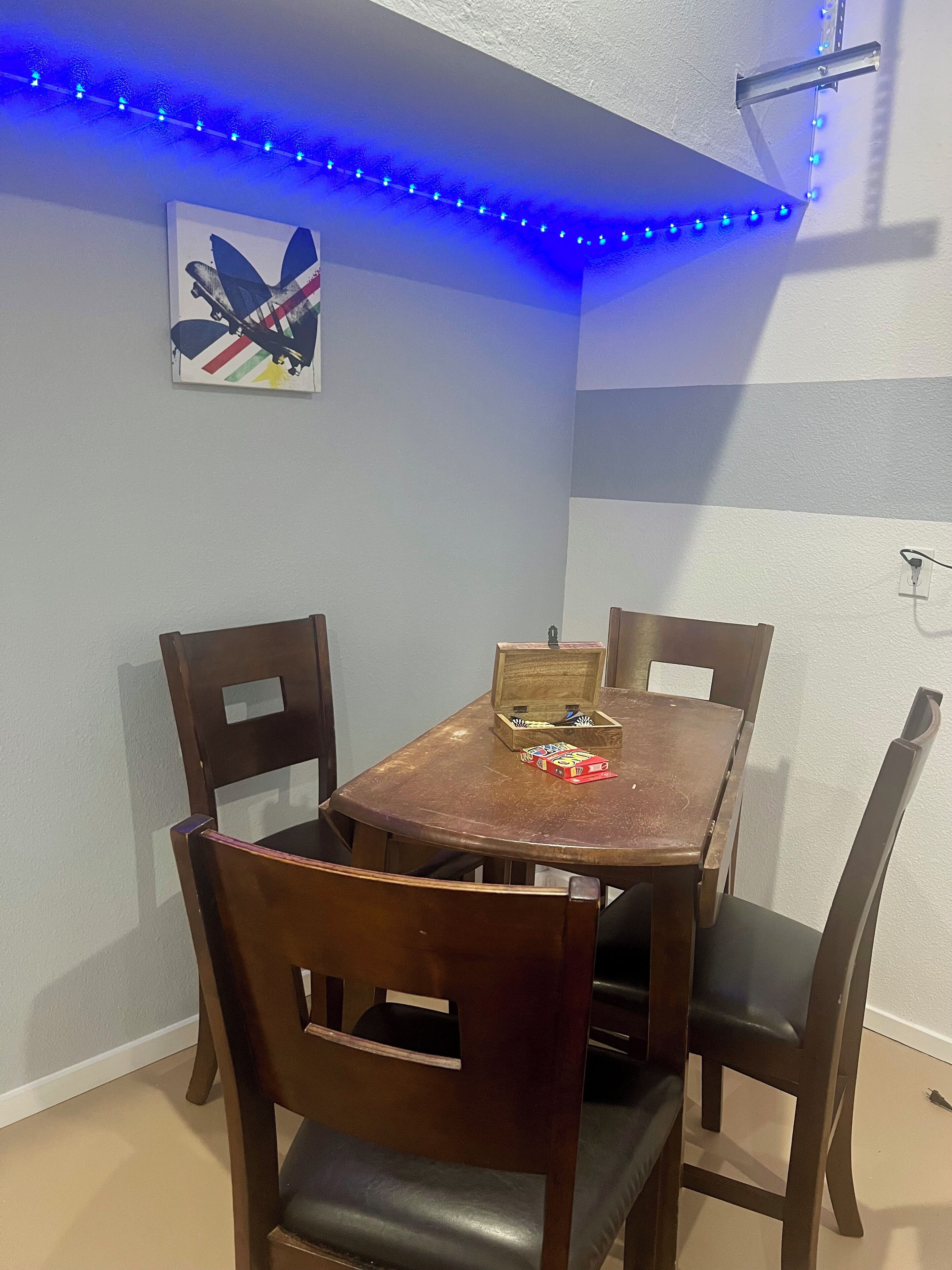 Ein Essbereich mit Holztisch und -stühlen, einem Bild an der Wand und blauen LED-Leuchtstreifen an der Decke.